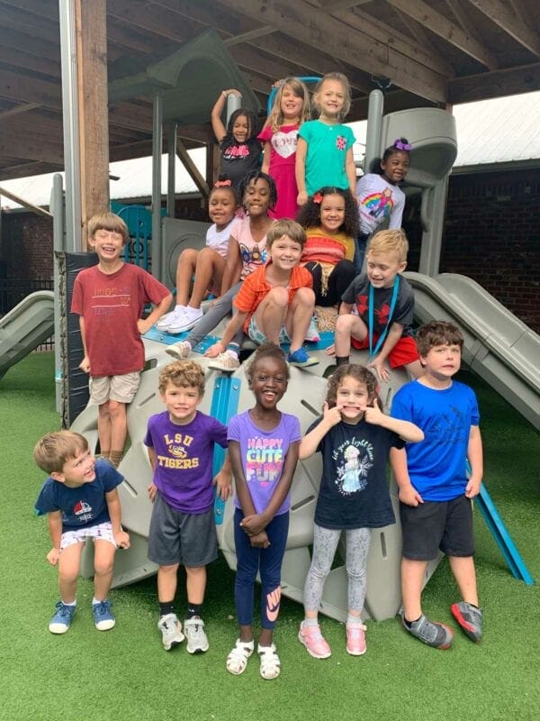 MadisonPreschool-Home Group of smiling children sitting on and standing around playground structure